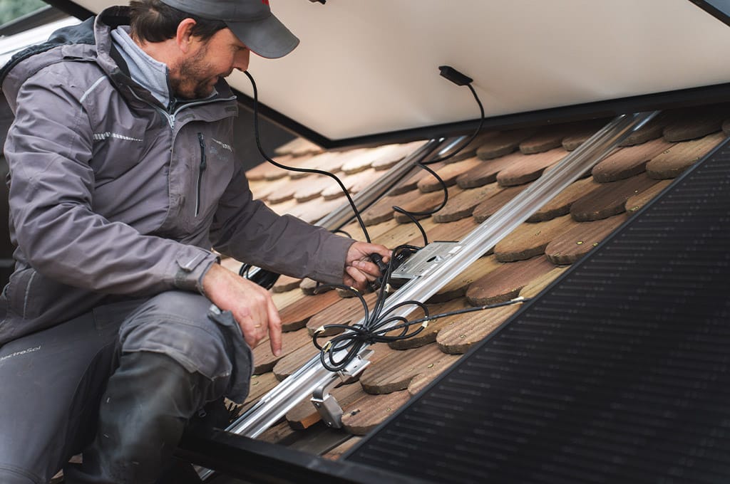 Installateur PV sur le toit d'une maison en train de raccorder les panneaux solaires.